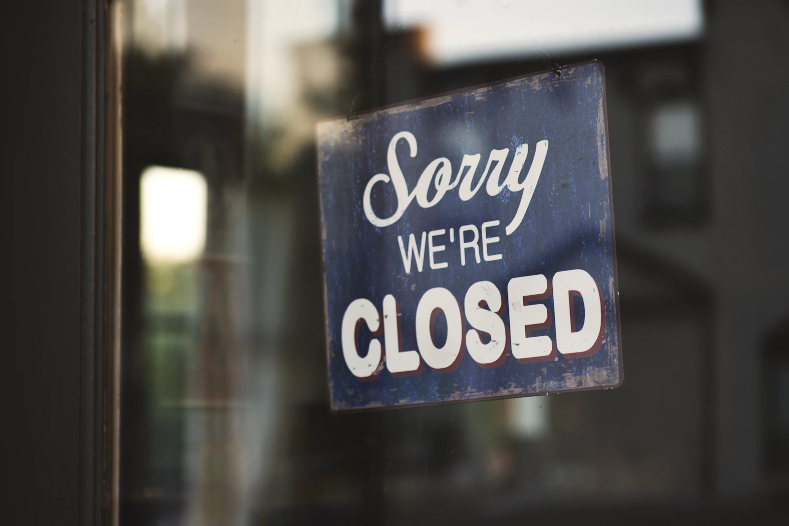 A Sorry We're Closed sign hanging in a glass shop door, the online equivalent of a business whose domain has lapsed
