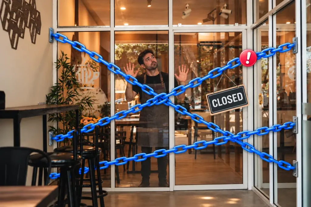 Cafe owner standing behind a glass door chained shut with blue chain links and a Closed sign, illustrating Meta's two-link limit cutting businesses off from their customers
